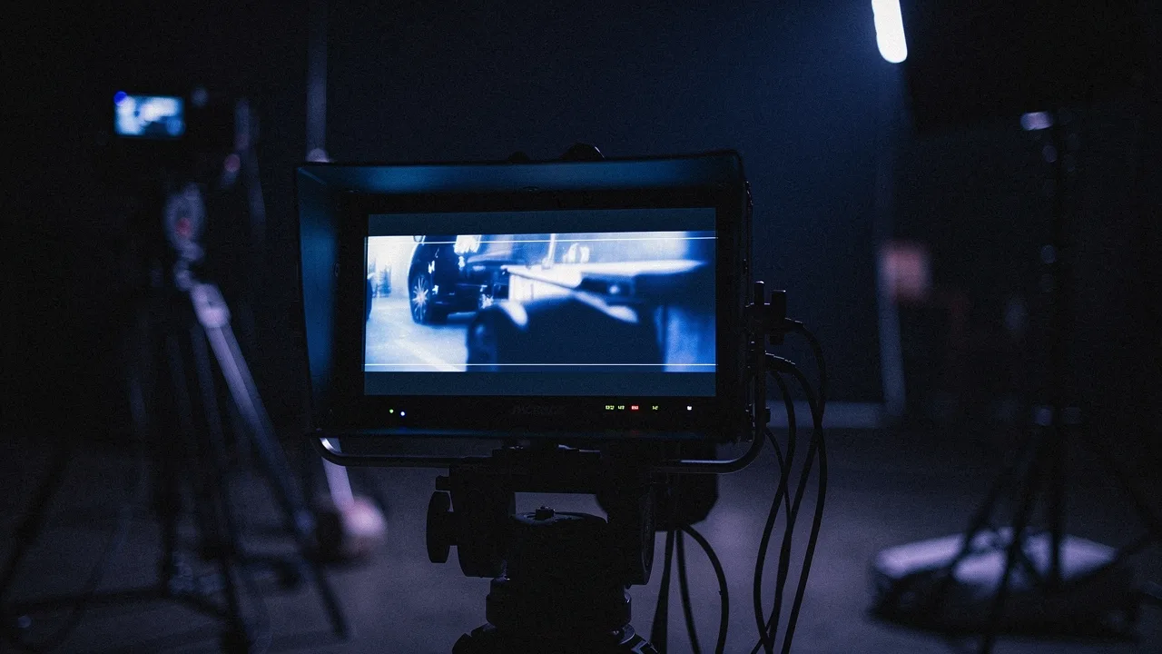 A director's monitor showing a blue-tinted frame, cables and stands in the dark